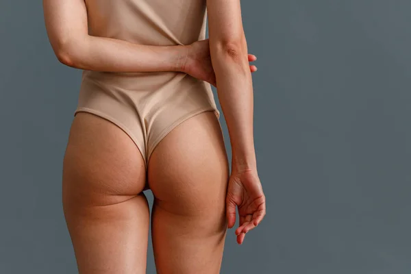 Achteraanzicht van afgezwakte billen van vrouw in beige bodysuit staan geïsoleerd over grijze studio achtergrond — Stockfoto