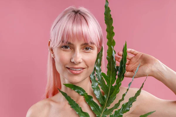 Retrato de mujer desnuda hermosa con el pelo rosa sonriendo a la cámara, posando con hoja de planta aislada sobre fondo de estudio rosa — Foto de Stock