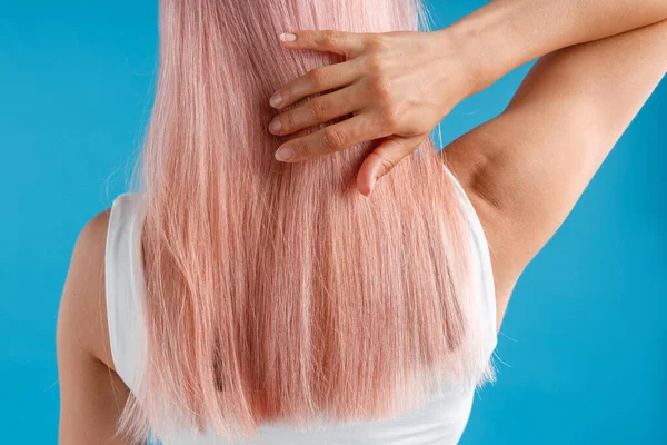 Close-up shot van vrouw aanraken van haar gladde gestroomlijnde natuurlijke lange roze geverfd haar terwijl poseren geïsoleerd over blauwe studio achtergrond — Stockfoto