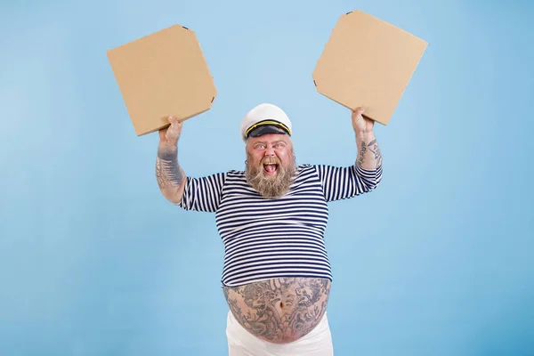 身穿水手服装超重的快乐男人拿着一盒浅蓝色背景的空白披萨 — 图库照片