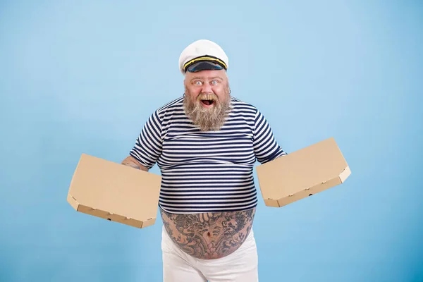 Opgewonden man met overgewicht in matroos kostuum houdt dozen pizza op lichtblauwe achtergrond — Stockfoto