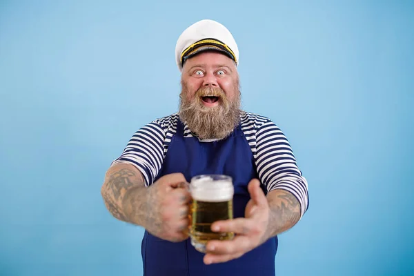 Happy dikke man in matrozenpak biedt mok van vers bier op lichtblauwe achtergrond — Stockfoto