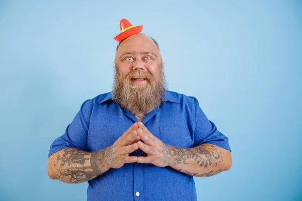 Positieve man met overgewicht draagt kleine sombrero en blauw shirt staat op lichtblauwe achtergrond — Stockfoto