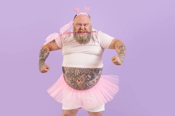 Brutale zwaarlijvige man in fee kostuum houdt magische stok in tanden op paarse achtergrond — Stockfoto