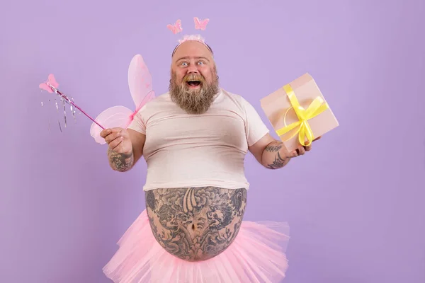 Radosny otyły człowiek w stroju bajki posiada pudełko prezentów i magiczny kij na fioletowym tle — Zdjęcie stockowe