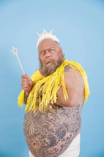 Twijfel plus size man met kroon en magische stok poseert op lichtblauwe achtergrond — Stockfoto