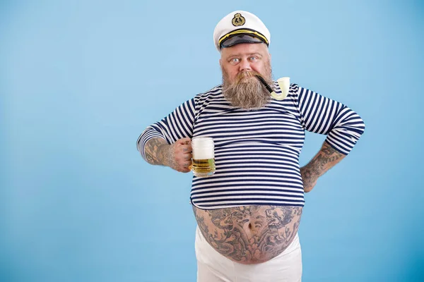 Dashing vet matroos met baard en rookpijp houdt schuimig bier op lichtblauwe achtergrond — Stockfoto