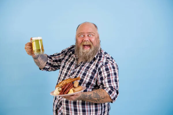 Aufgeregter Mann mit Übergewicht hält leckeres Essen und ein Glas Bier auf hellblauem Hintergrund — Stockfoto