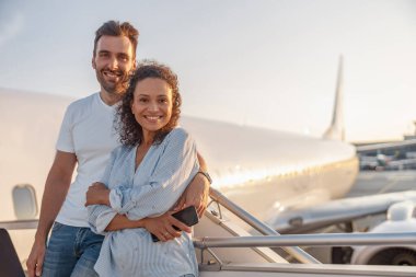 Mutlu bir çift turistin portresi, kadın ve erkek gün batımında uçağa binmeye hazırlanırken heyecanlı görünüyorlar.