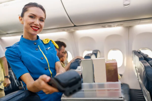 Ritratto di affascinante hostess di compagnia aerea che sorride alla telecamera, che tiene il terminale per il passeggero per effettuare un pagamento — Foto Stock