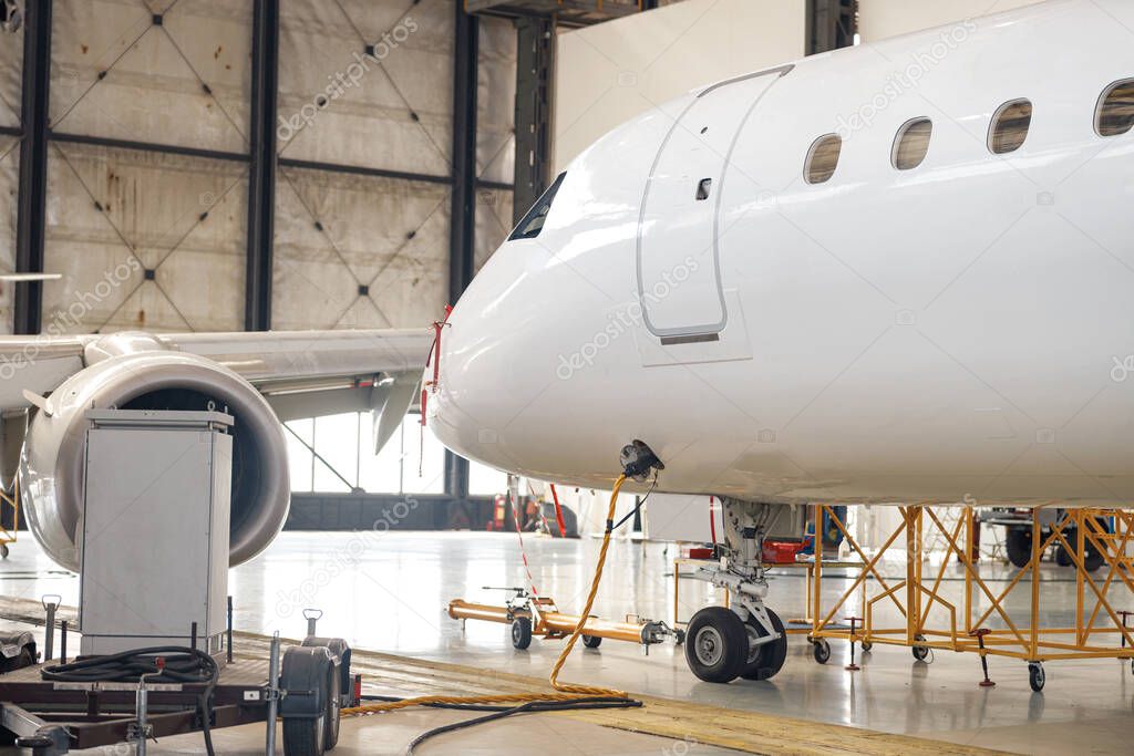 Modern new white passenger airplane on maintenance repair check in airport hangar indoors