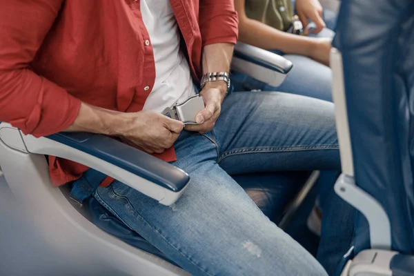 Високий кут зору чоловічого пасажира, що регулює і затягує ремінь безпеки на літаку, коли він тягне ремінь руками для безпечного польоту — стокове фото