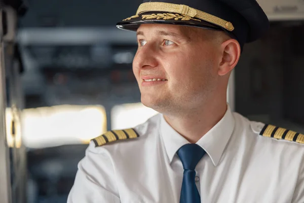 Nahaufnahme Porträt eines gut gelaunten männlichen Piloten in Uniform und Hut, der weglächelt, während er posiert, im Flugzeug stehend — Stockfoto