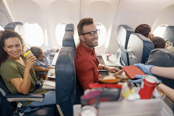 Šťastní pasažéři se usmívají, zatímco letuška servíruje oběd na palubě — Stock fotografie