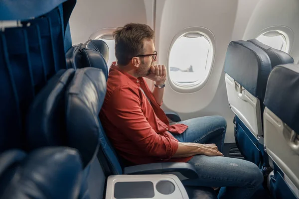 Penzitivní běloch v neformálním oblečení, odpočívající v letadle, sedící a dívající se z okna — Stock fotografie