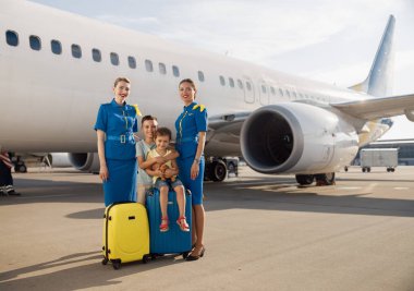 Gün ortasında büyük bir uçağın önünde oturan ve güzel hosteslerle birlikte kameraya gülümseyen iki çocuğun uzun metrajlı görüntüsü.