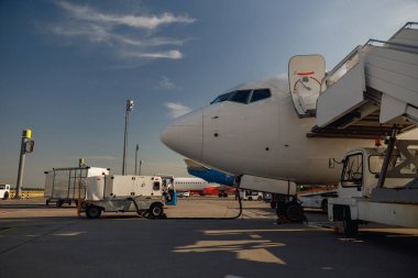 Hava alanında gündüz vakti yakıt ikmali yapan beyaz bir uçak. Uçak detayları