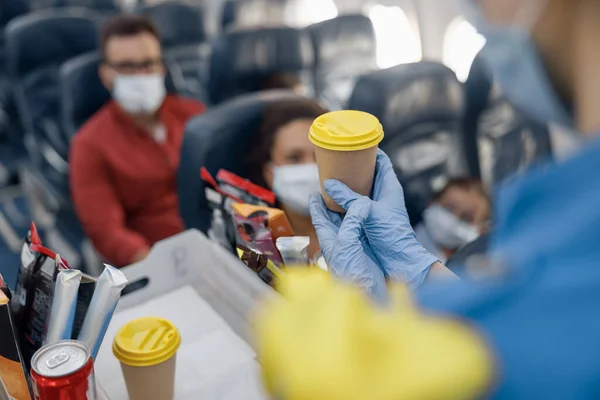 Detailní záběr rukou v ochranných rukavicích letušky servírující nápoje cestujícím na palubě. Cestování letadlem během pandemie Covid19 — Stock fotografie