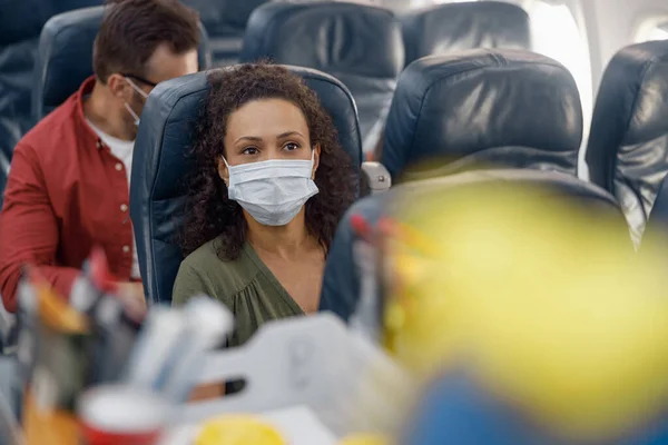 Žena cestující na sobě ochranné masky čeká na letušku objednat kávu během letu — Stock fotografie