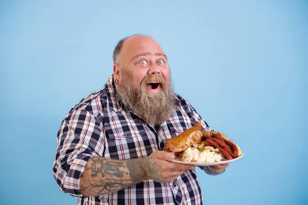 Happy mollige man houdt plaat van vet voedsel poseren op lichtblauwe achtergrond — Stockfoto