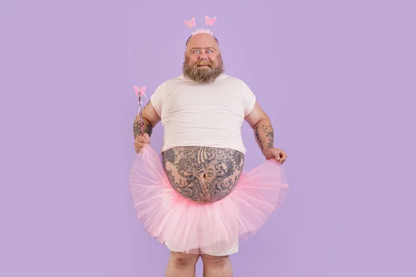 Opgewonden zwaarlijvige volwassen man dragen fee pak houdt chiffon rok op paarse achtergrond — Stockfoto