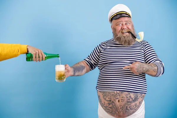 Vrolijke zeeman met overgewicht houdt mok, terwijl de vrouw schenkt bier op lichtblauwe achtergrond — Stockfoto