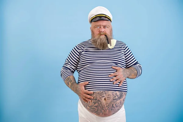 Übergewichtiger Mann mittleren Alters im Matrosenkostüm hält Hände auf Bauch vor hellblauem Hintergrund — Stockfoto