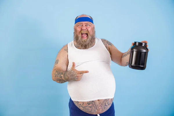 Fröhlicher fettleibiger Mann präsentiert große Flasche Nährstoffergänzung auf hellblauem Hintergrund — Stockfoto