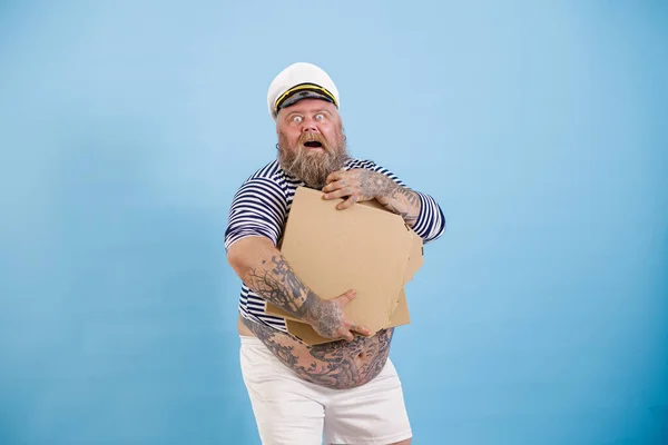 행복 한 수염을 가진 비만 한 선원 이 밝은 푸른 배경 위에 포즈를 취하고 있는 텅 빈 피자 상자를 들고 있다 — 스톡 사진