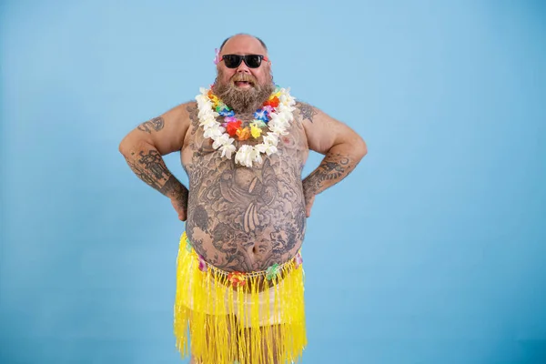 Happy man met overgewicht en getatoeëerde buik in decoratieve gras rok op lichtblauwe achtergrond — Stockfoto