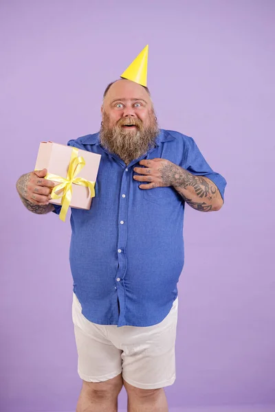 Homem surpreso com excesso de peso em camisa azul apertado detém caixa de presente posando em fundo roxo — Fotografia de Stock