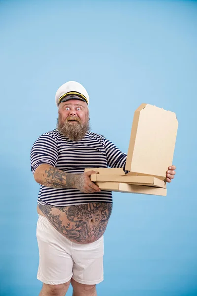 Gelukkig verrast mollige man zeeman houdt open doos van pizza op licht blauwe achtergrond — Stockfoto