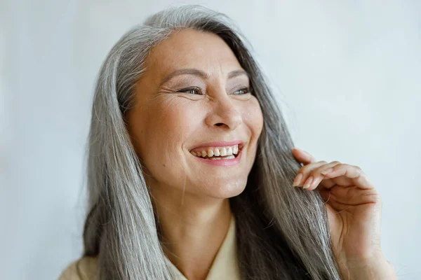 Joyful Asian woman with natural grey hair smiles on light background — Stock Photo, Image