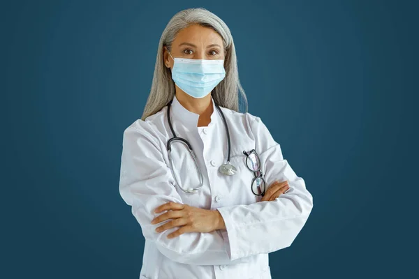 Γκρι μαλλιά Ασιάτης γιατρός με ιατρική μάσκα στέκεται σε μπλε φόντο — Φωτογραφία Αρχείου