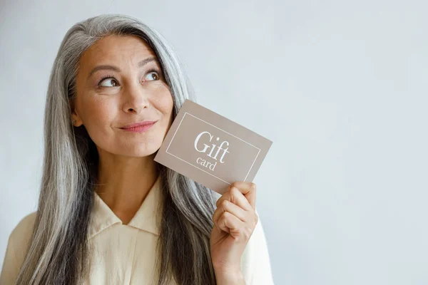 在演播室里，一个白发苍苍的亚洲女人近面拿着礼品卡 — 图库照片