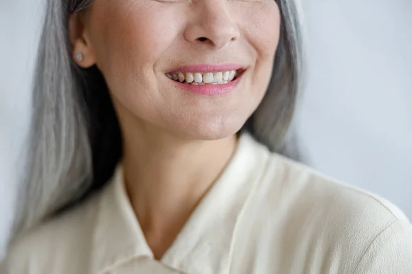 Positive mature lady smiles showing healthy teath on light background in studio closeup — Stock Photo, Image