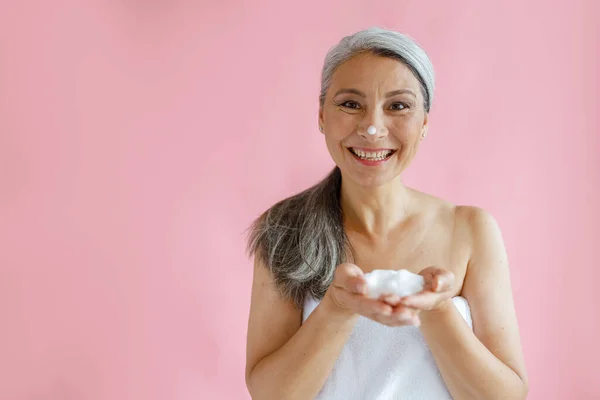 Jouful silver haired Asian lady with handful of foam stands on pink background — Stock Photo, Image