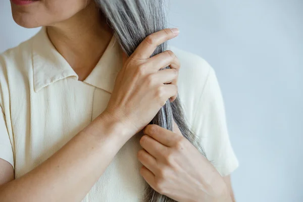 Middelbare leeftijd dame in elegante blouse met rechte grijze haren poseert op lichtgrijze achtergrond — Stockfoto