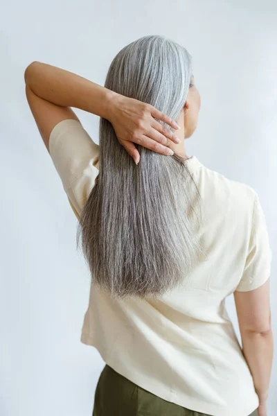 Middle aged woman adjusts long loose hoary hair on light grey background — Stock Photo, Image