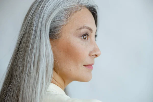 Mulher asiática de meia idade com belo cabelo em linha reta hoary no fundo cinza claro — Fotografia de Stock