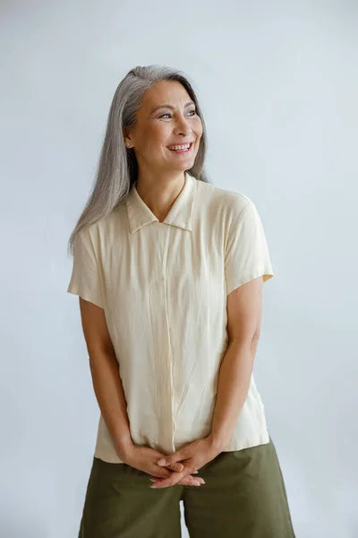 Vreugdevolle middelste dame in stijlvolle casual kleding staat op lichtgrijze achtergrond — Stockfoto