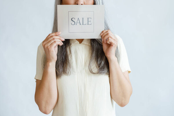 Mature woman with long grey hair holds Sale sign standing in studio closeup