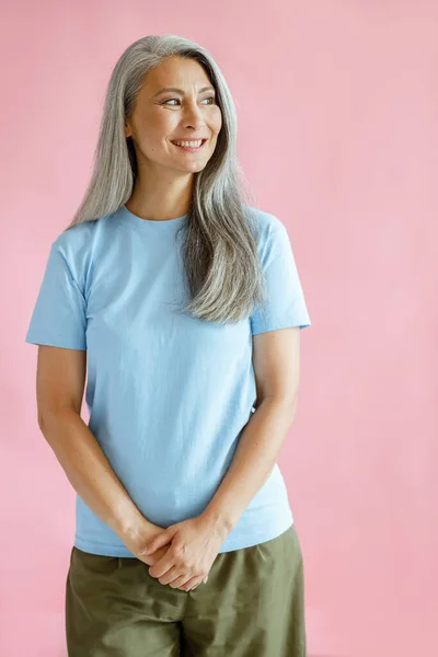 Feliz mujer asiática de mediana edad de pelo plateado en camisetas de pie sobre fondo rosa —  Fotos de Stock