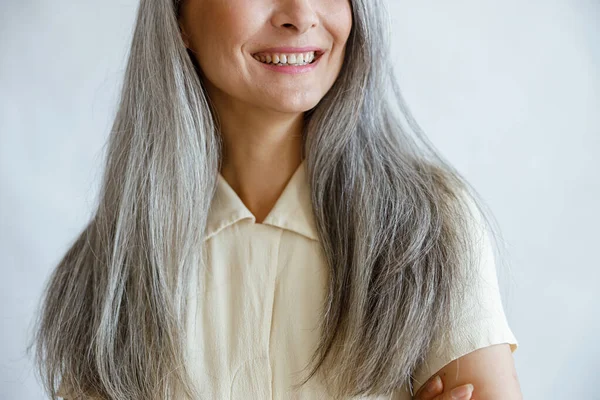 긴 은색 머리의 중년 여성은 밝은 회색 배경에 미소를 짓고 있다 — 스톡 사진