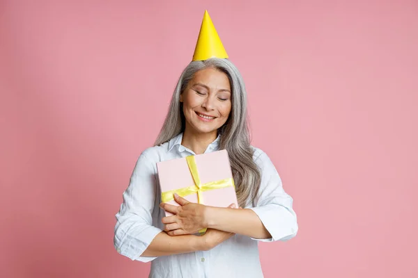 Glada mogen asiatisk kvinna med löst grått hår kramar presentförpackning poserar i studio — Stockfoto