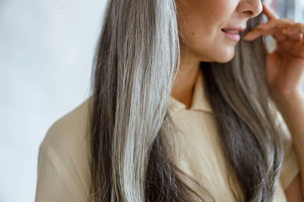 Middelaldrende kvinne med vakkert grått hår poserer på lysegrå bakgrunn – stockfoto