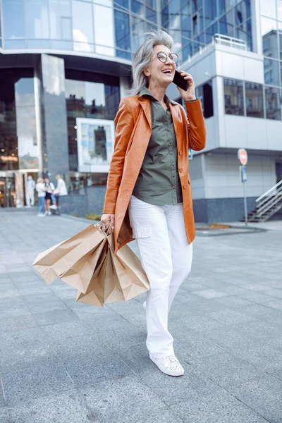 시내 거리에서 휴대폰으로 쇼핑 강연을 하고 있는 쾌활하고 장성 한 여자 — 스톡 사진