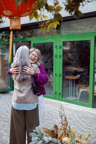 Joyful senior dame in warme jas knuffels lange haren beste vriend vergadering op straat — Stockfoto