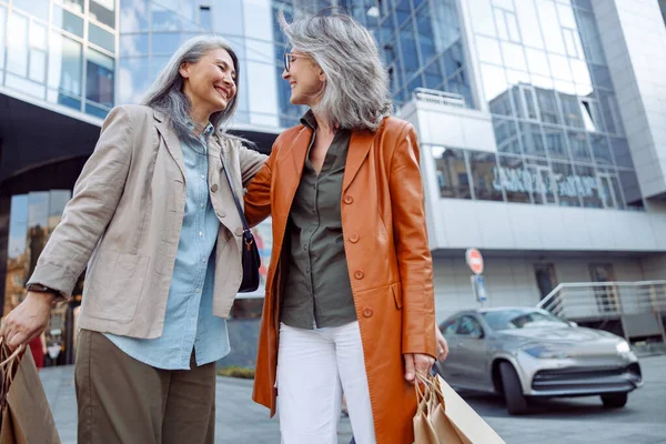 웃고 있는 회색 머리의 아시아 여자 가 시내 거리에서 쇼핑백을 들고 있는 성숙 한 부인을 안고 있다 — 스톡 사진