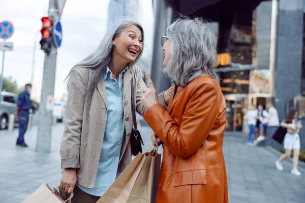 在现代城市街道上，穿着时髦服装、头戴购物袋的快乐的成熟女性正在谈论 — 图库照片